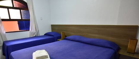 Une chambre d’hôtel avec deux lits simples, chacun recouvert d’une courtepointe bleue et doté d’oreillers, ainsi qu’une tête de lit en bois et une fenêtre avec des rideaux.