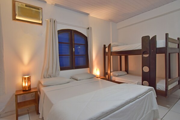 A bedroom with a single bed, a window with curtains, a bedside table with a lamp, and a bunk bed. - Estalagem 11 (Arraial do Cabo)