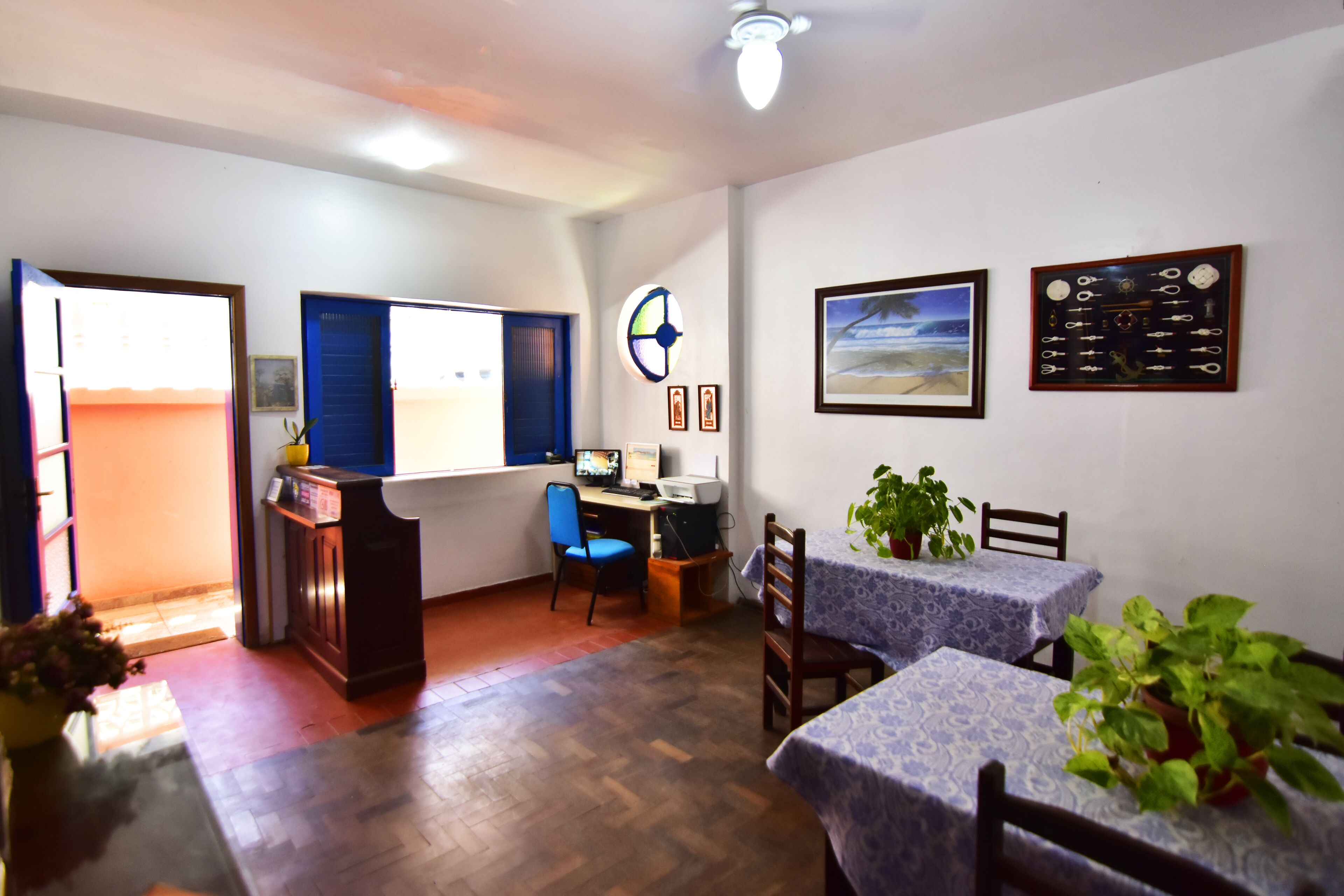 A room with a desk, computer, chairs, and tables with plants.