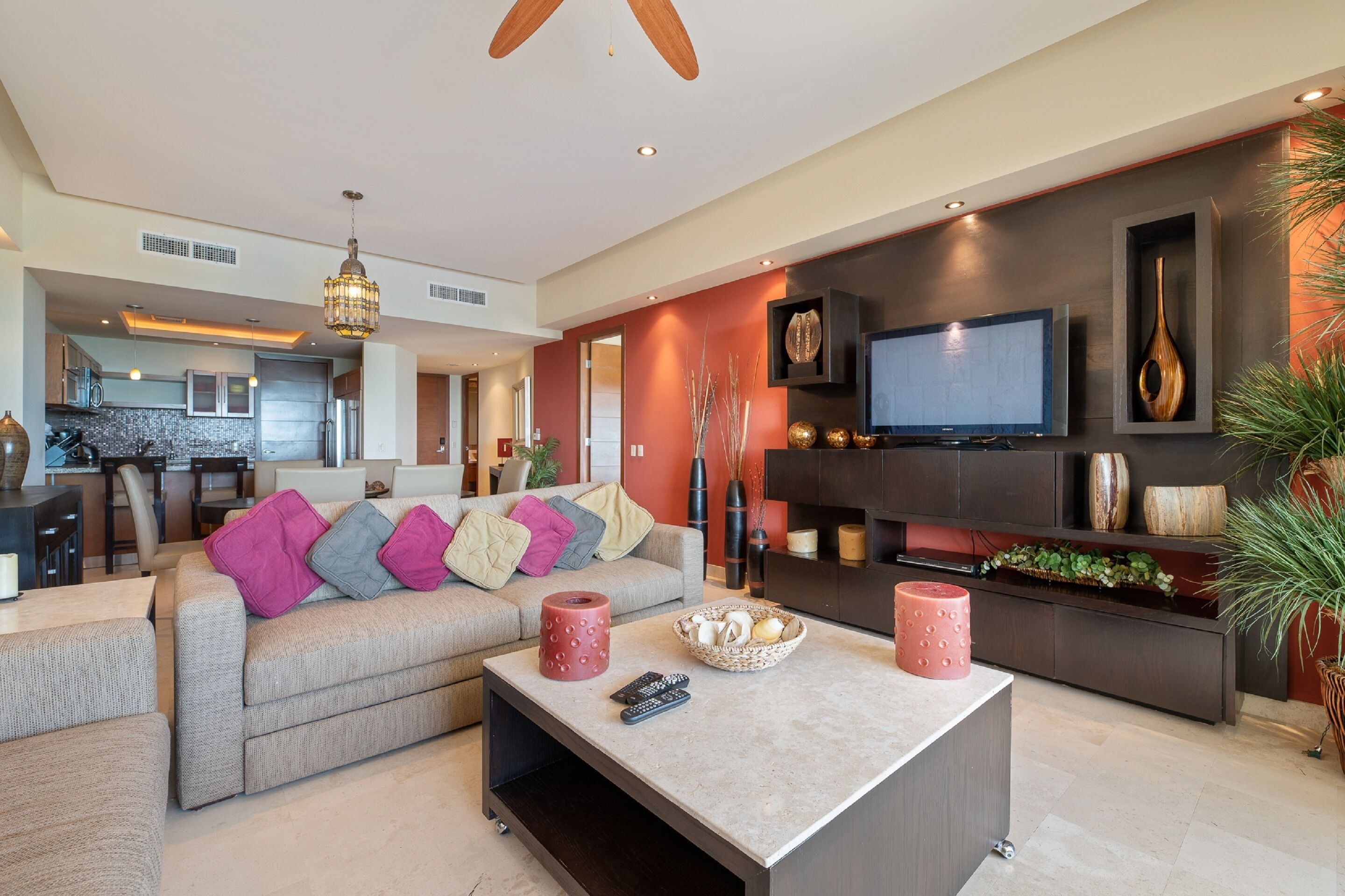 A modern living room with a sofa, coffee table, and TV. There is a kitchen in the background.