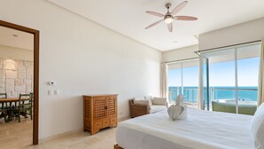 Quarto com uma cama grande, um ventilador de teto, um armário de madeira, uma cadeira de vime e vista para o mar.