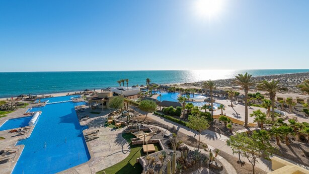 Um resort com várias piscinas, palmeiras e uma área de praia.