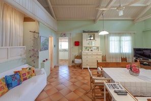 A cozy living room with a sofa, dining table, and chairs. There is a television and a cabinet with glass doors. - Beautiful mini eco farmhouse (Marathon)
