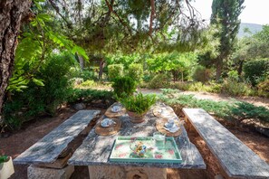A stone table with a floral tray, surrounded by a lush garden with various plants and trees. - Beautiful mini eco farmhouse (Marathon)