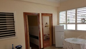 A compact kitchen with a refrigerator, a dining table with chairs, and a window with blinds. - Casa Armando y Mercy (Havana)