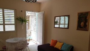 A room with a round dining table, a sofa with colorful cushions, and a window with blinds. - Casa Armando y Mercy (Havana)