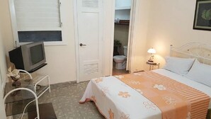 A bedroom with a bed, bedside table, lamp, and a television on a small table. - Casa Armando y Mercy (Havana)
