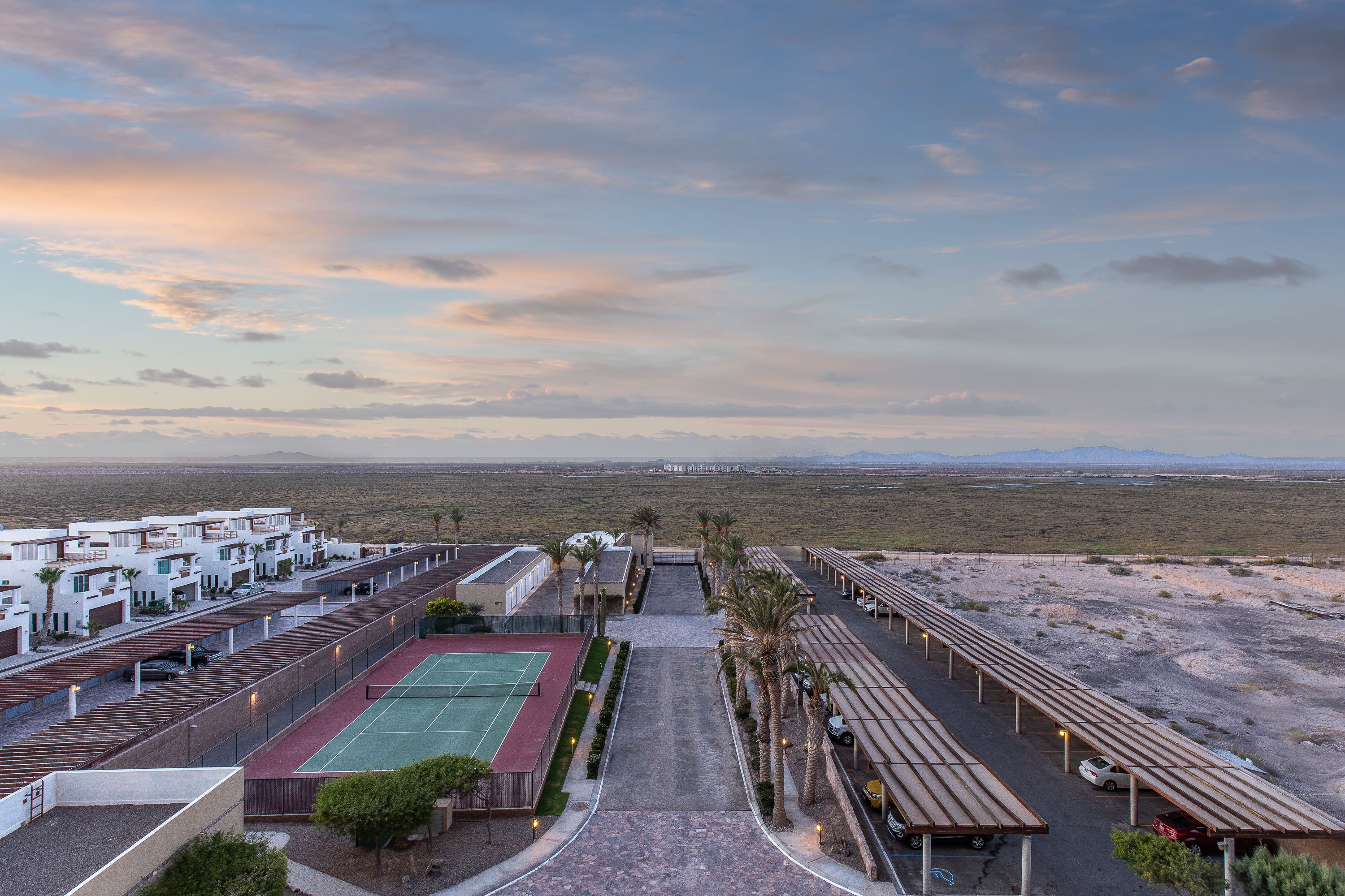 A hotel with a tennis court, palm trees, and a desert landscape in the background.