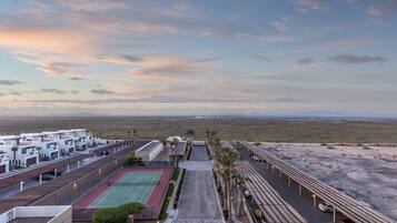 A hotel with a tennis court, palm trees, and a desert landscape in the background.