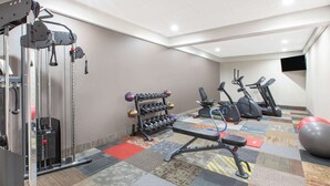 A gym with exercise equipment, a bench, and a wall-mounted TV. - Days Inn & Suites Grand Rapids Near Downtown (Grand Rapids)