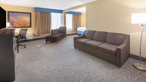 A hotel room with a sofa, armchair, and a desk with a chair. - Days Inn & Suites Grand Rapids Near Downtown (Grand Rapids)