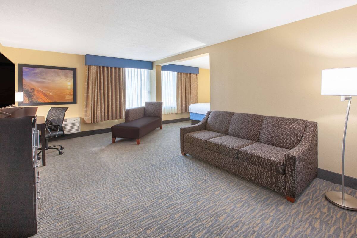 Una habitación de hotel con sofá, sillón y escritorio con silla.