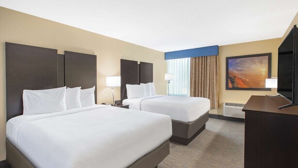 A hotel room with two beds, a desk, a TV, and a painting on the wall. - Days Inn & Suites Grand Rapids Near Downtown (Grand Rapids)