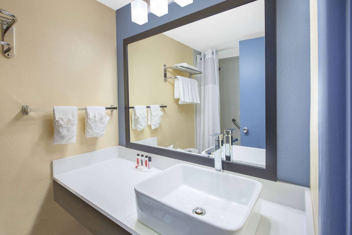 Un baño con un lavamanos blanco, un espejo grande y un perchero con varias toallas.