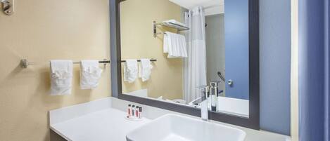 A bathroom with a white sink, a large mirror, and a towel rack with multiple towels.