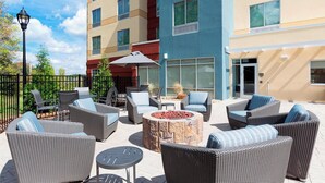 An outdoor patio area with wicker furniture, a stone fire pit, and a view of a multi-story building. - Fairfield Inn & Suites by Marriott Shelby (Shelby)