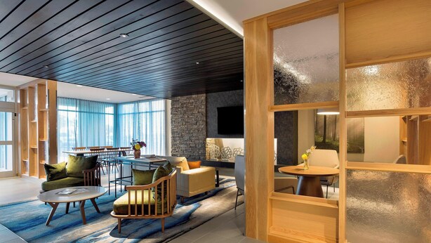 A modern living room with a dining area, large windows, a stone wall, and a fireplace. - Fairfield Inn & Suites by Marriott Shelby (Shelby)