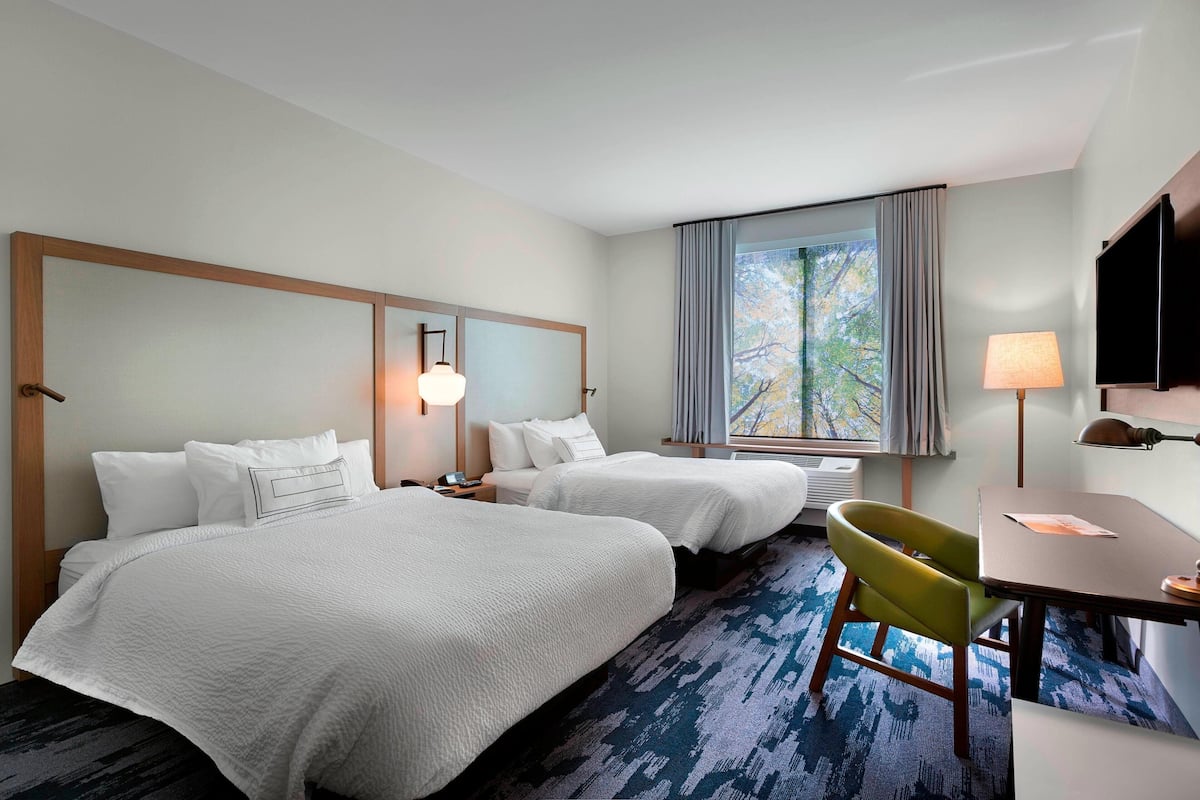 A hotel room with two beds, a desk, a chair, a TV, and a window with curtains.
