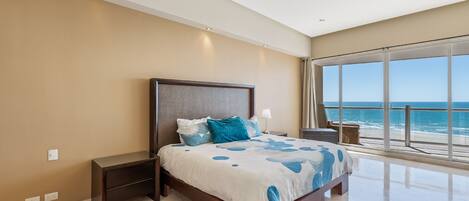 A bedroom with a large bed, a nightstand, a ceiling fan, and a view of the ocean.