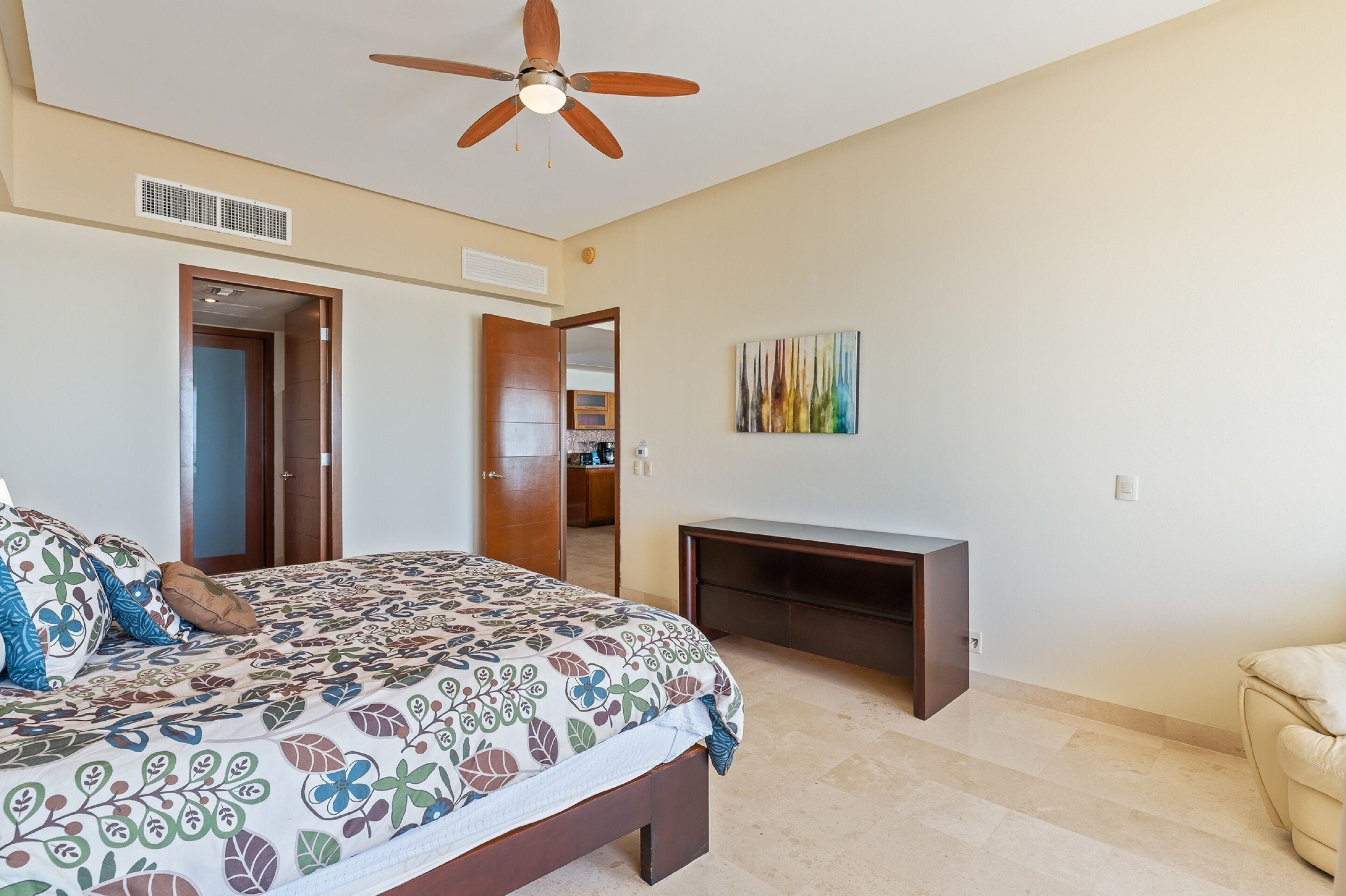 A bedroom with a bed, a ceiling fan, a TV stand, and a door leading to a bathroom.