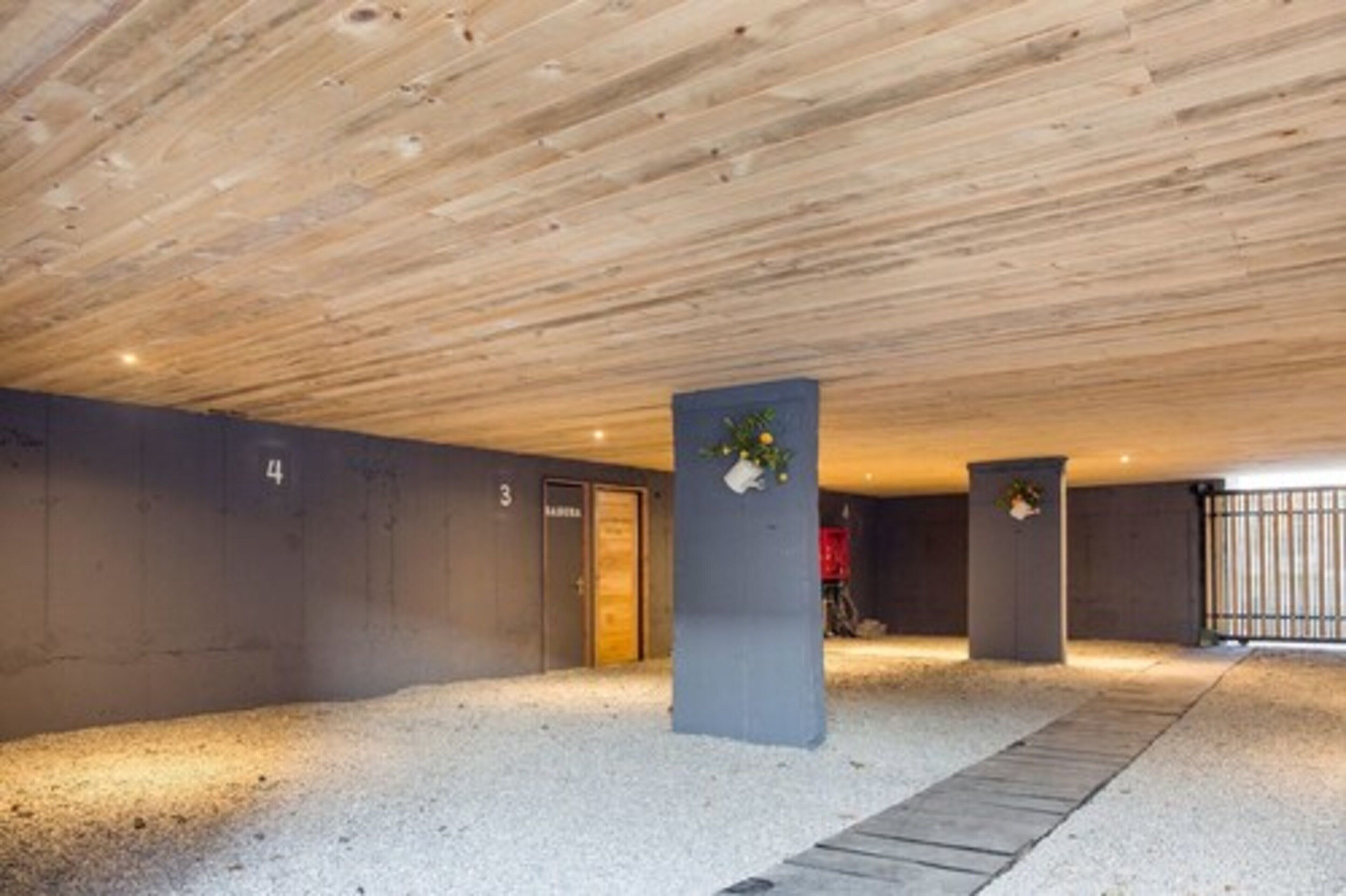 A modern indoor parking area with a wooden ceiling, numbered parking spaces, and concrete pillars with plants.