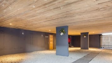A modern indoor parking area with a wooden ceiling, numbered parking spaces, and concrete pillars with plants.