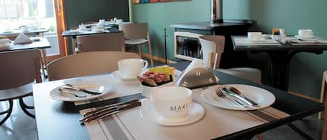 Un comedor con mesas dispuestas para dos, cada una con platos, cubiertos y un bol de fruta.