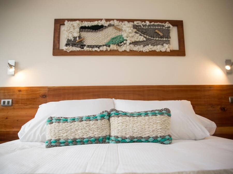 A neatly made bed with white linens and two decorative pillows, a wooden headboard, and a wall-mounted artwork.
