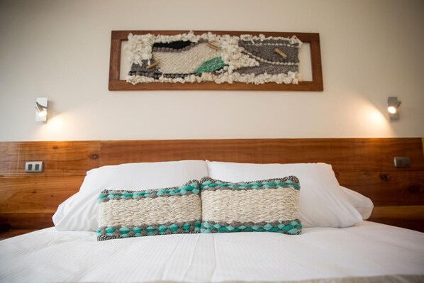 A neatly made bed with white linens and two decorative pillows, a wooden headboard, and a wall-mounted artwork. - Maki Hotel (Pucón)