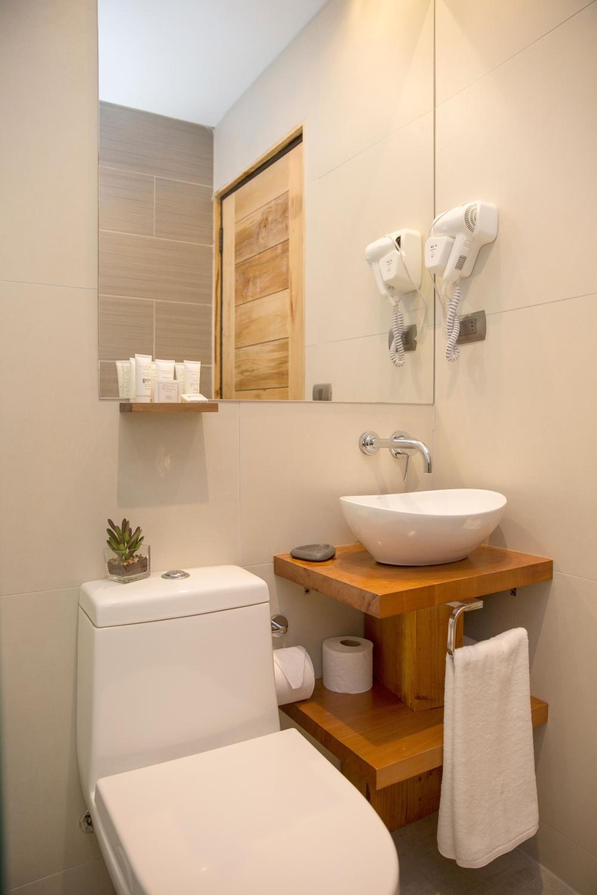 Une salle de bain moderne avec un lavabo blanc, un meuble-lavabo en bois et deux sèche-cheveux fixés au mur.