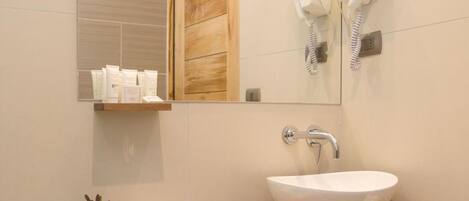A modern bathroom with a white sink, wooden vanity, and two hair dryers mounted on the wall.