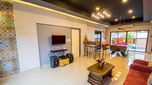 A modern living room with a flat-screen TV, a coffee table with flowers, a red sofa, and a pool table. - Baan Por Jai HuaHin Pool Villa (Hua Hin)
