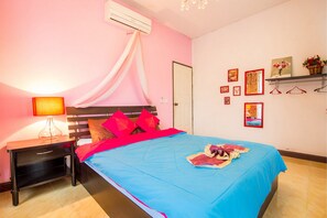 A bedroom with a bed, a nightstand, an air conditioner, and a wall with framed pictures and a shelf. - Baan Por Jai HuaHin Pool Villa (Hua Hin)