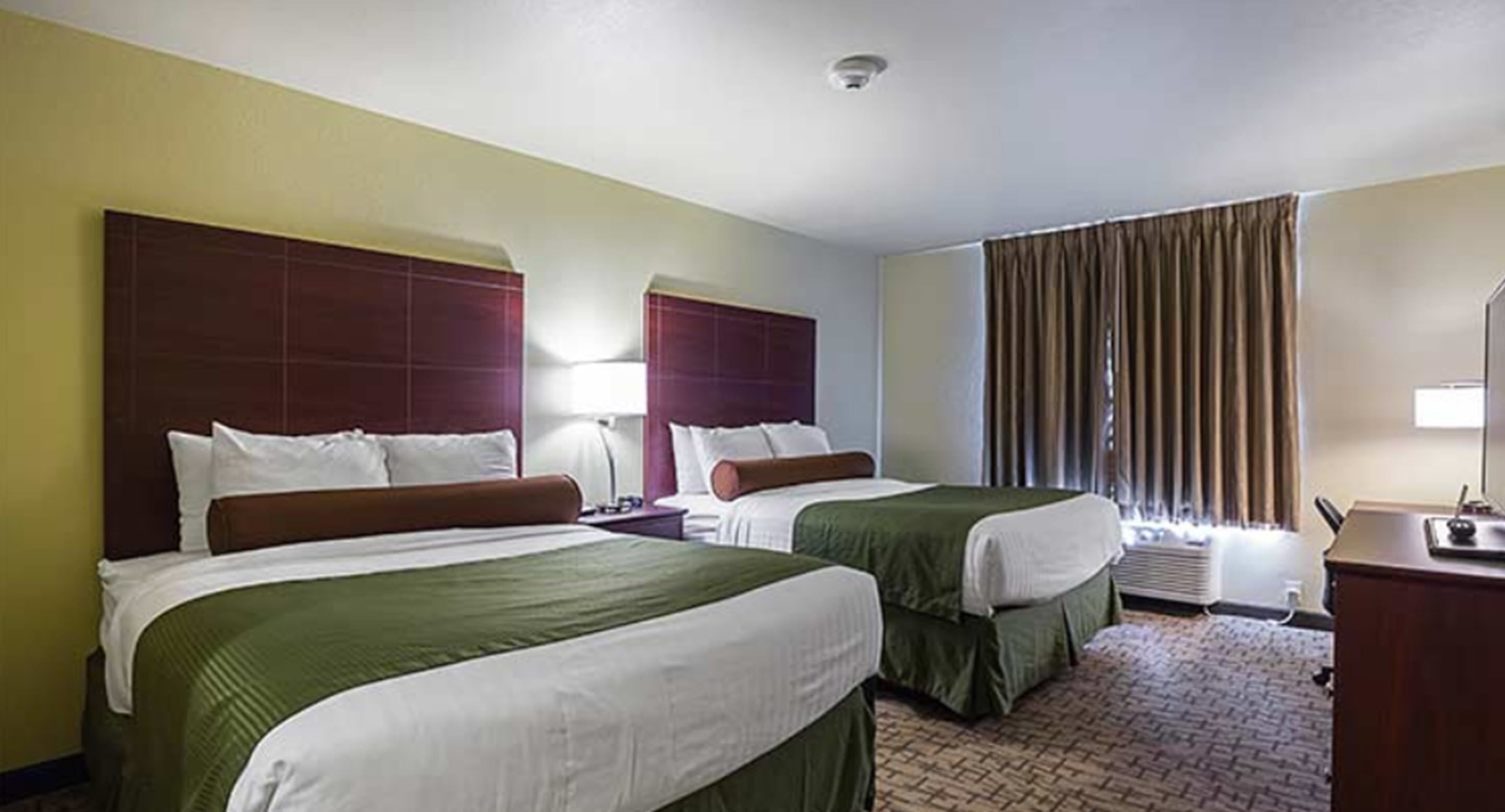 Une chambre d’hôtel avec deux lits, un bureau et une fenêtre avec des rideaux.