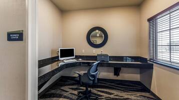 A business center with a desk, computer, chair, and a mirror on the wall.