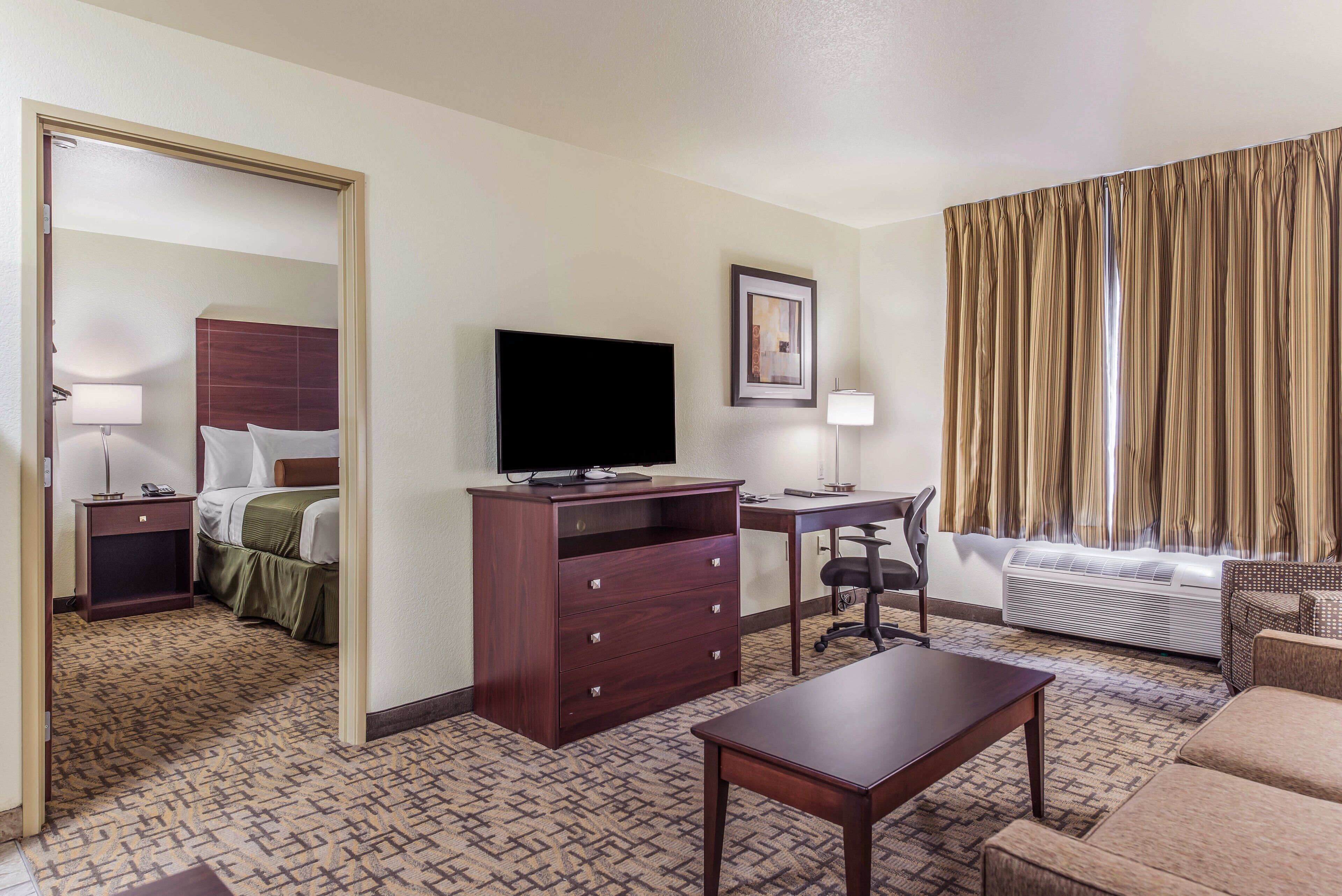 A hotel room with a bed, a desk, a television, a chair, a sofa, and a window with curtains.