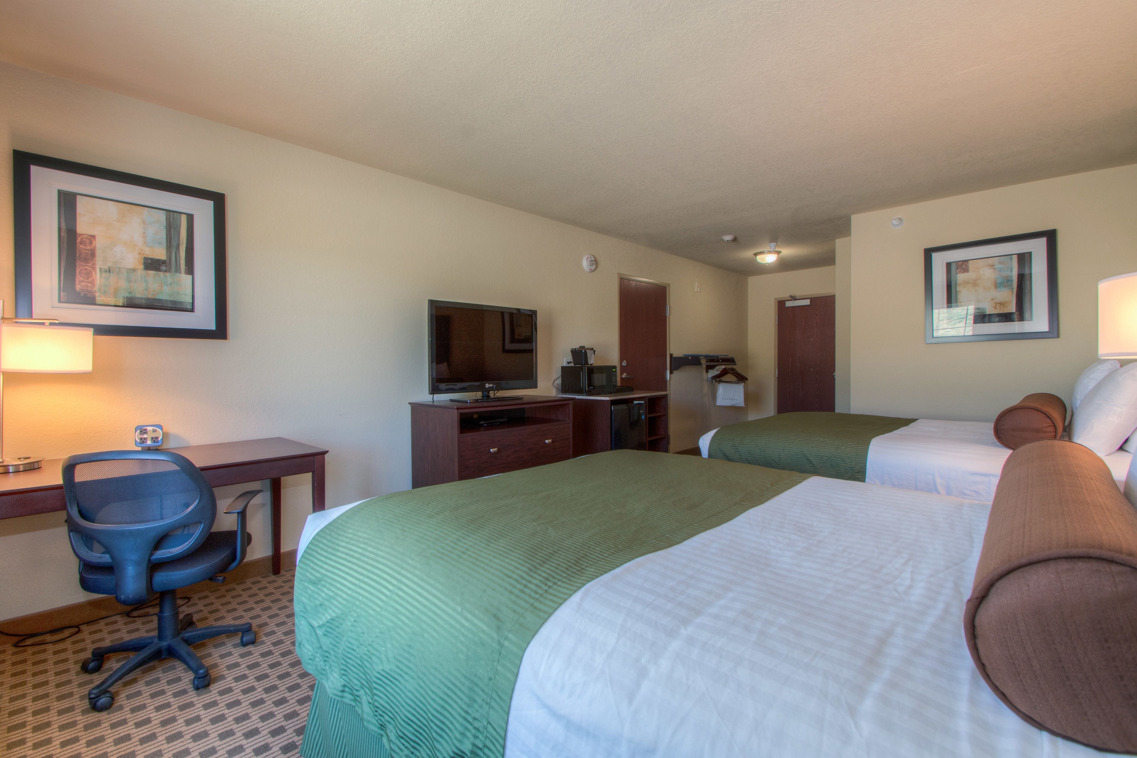 A hotel room with two beds, a desk with a chair, a television, and a microwave.