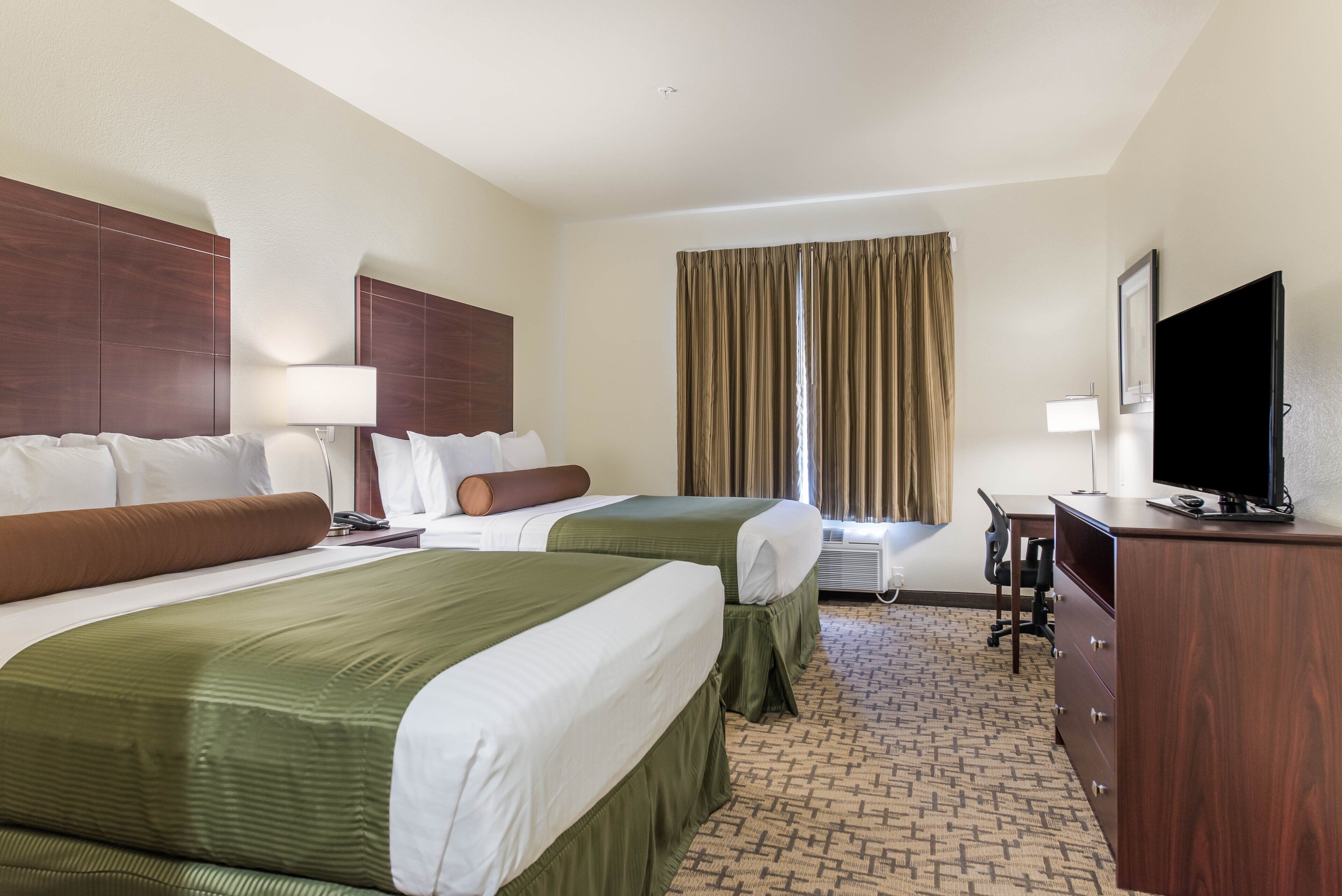 Quarto de hotel com duas camas, uma escrivaninha, uma televisão e uma janela com cortinas.