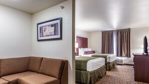 Una habitación de hotel con un sofá marrón, dos camas con ropa de cama verde y roja, un escritorio y un cuadro en la pared.
