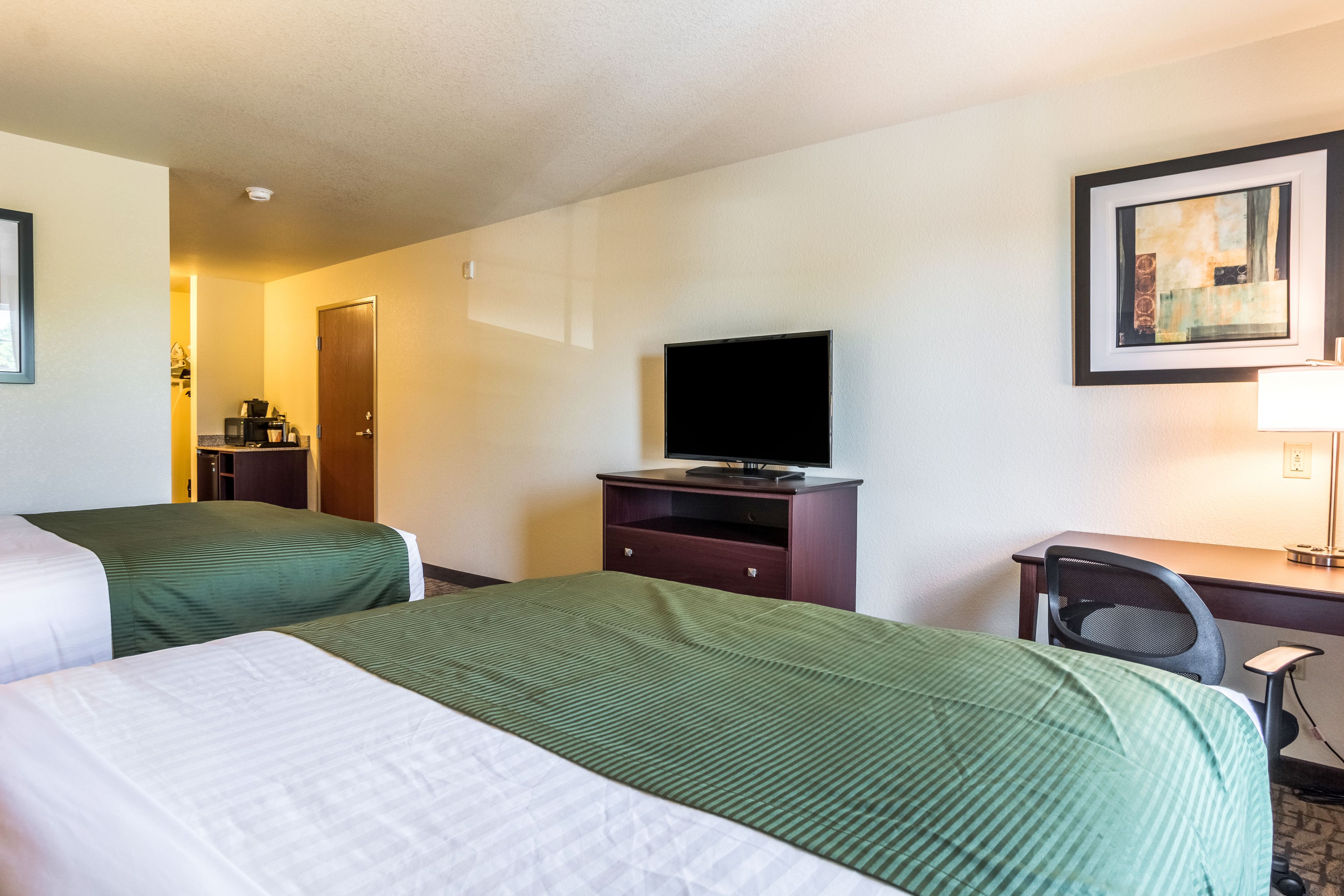 A hotel room with two beds, a desk, a chair, a television, and a framed picture on the wall.