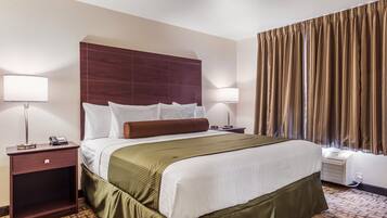A hotel room with a large bed, two bedside tables, a nightstand, a wall-mounted lamp, and a window with curtains.