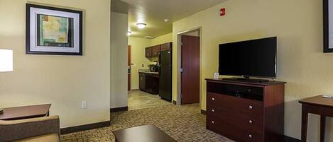 Habitación de hotel con kitchenette, televisor de pantalla plana, cómoda de madera y un cuadro enmarcado en la pared.