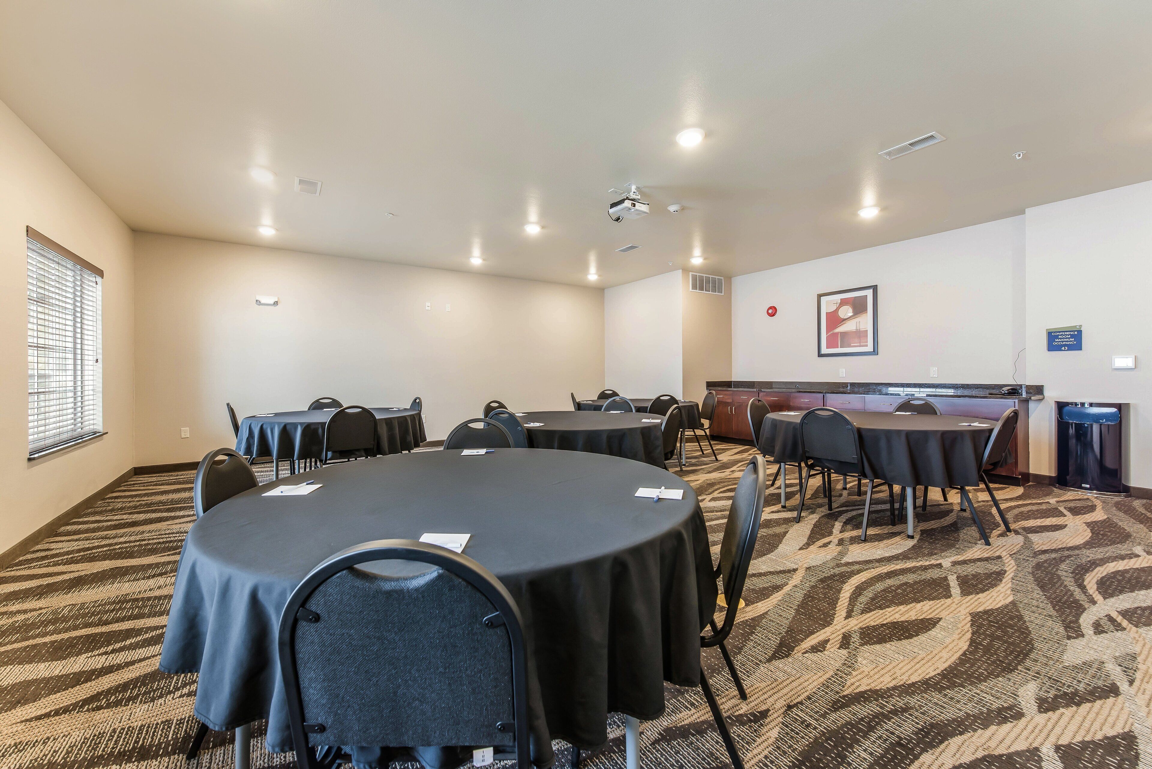 Una sala conferenze con tavoli rotondi, sedie, un proiettore e pavimento rivestito di moquette.