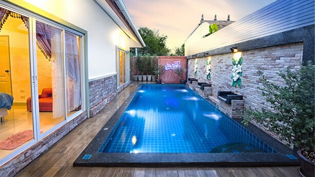 Ein Schwimmbad mit Holzterrasse, einer Ziegelwand und einer Glastür zu einem Raum mit einem roten Stuhl.
