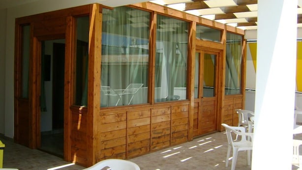 A wooden-paneled room with large windows, white plastic chairs, and a table. - Oasi B&B (Porto Cesareo)
