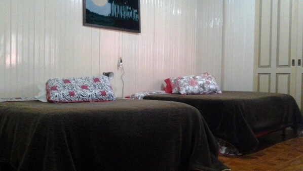 Una habitación con dos camas, cada una con una almohada estampada y un edredón oscuro. Un televisor está montado en la pared sobre las camas.