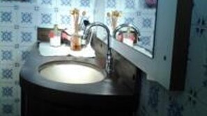 Un baño con un lavamanos redondo, un espejo encima y azulejos decorativos en la pared.