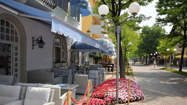 Ein Hotel mit Außenbestuhlung, Blumenbeet und roter Absperrschnur.