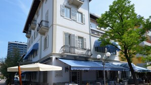 Ein Hotel mit Außenbereich, einer Pflasterterrasse und einem blauen Markisenvorzelt.