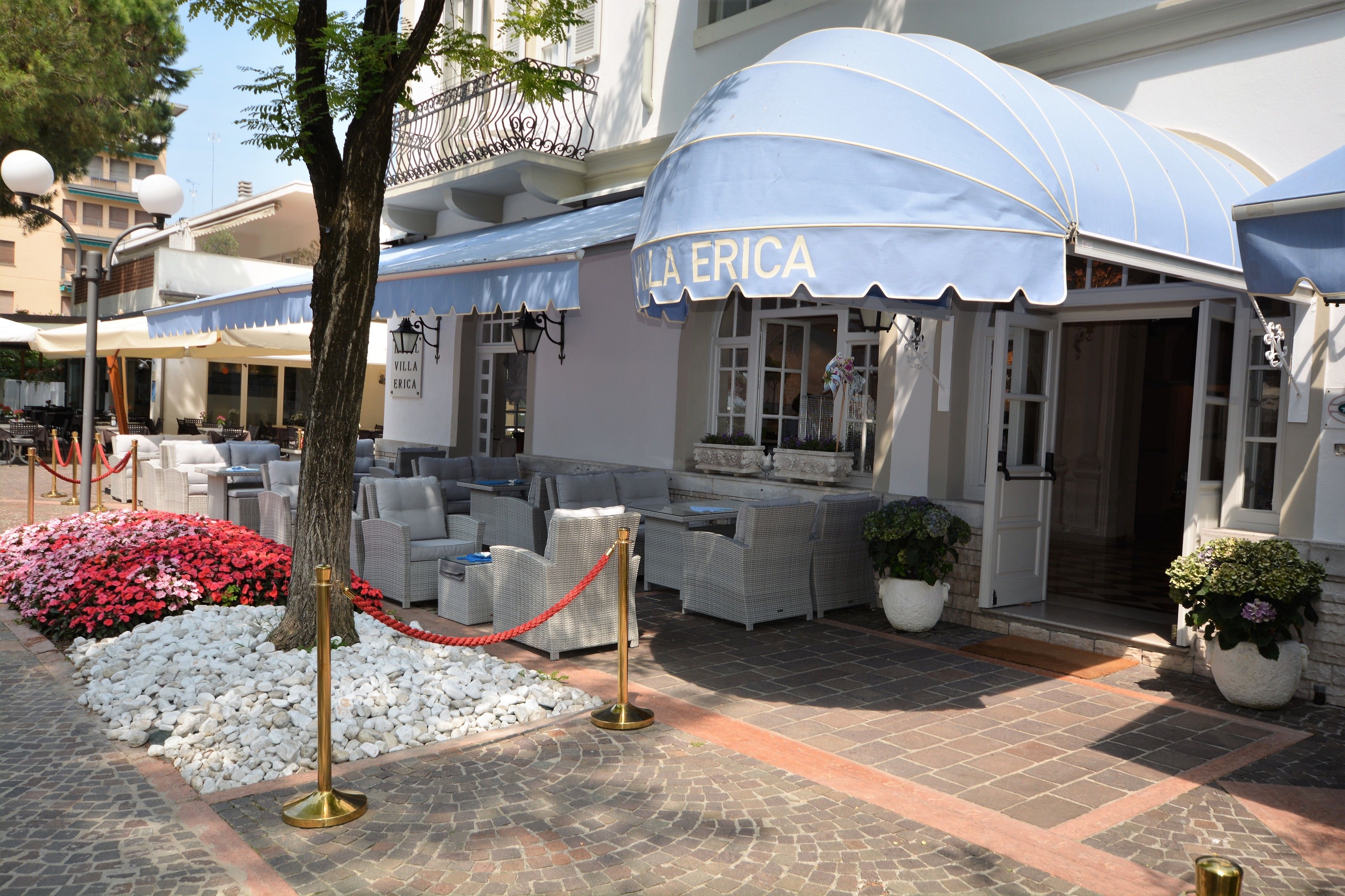 Ingresso di un hotel con posti a sedere all'aperto, una cordonata rossa e un aiuola con fiori bianchi.